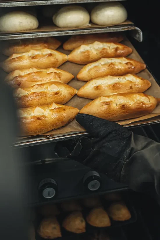 Trabajador de pastisseria tano sacando panes y empanadillas del horno